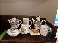 View of entire lot: two tea pots, three teacups, lidded trinket dish, and three small dishes arranged on wood surface