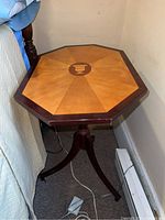 Full view of wooden octagonal side table next to bed, showing top design and pedestal base.