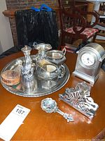 Photo showing a silver plated cream and sugar set, a decorative silver tone vase, a silver tone napkin holder with ornate design, a silver tone salt server with a decorative spoon, a round silver tray, and a silver tone clock made in China.