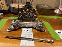 Ornate silver toned stationery stand with two ink wells and letter opener laid out for detail.