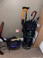 Metal umbrella stand with umbrellas, walking cane, and wire basket with folded umbrellas.