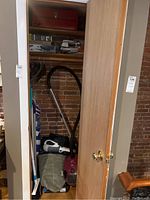 Closet with red Bissell canister vacuum with hose and attachments, handheld vacuum and broom handles visible.