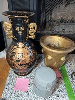 Photo of black vase with gold detailing, gold pottery bowl with coin wrappers, and grey pottery bowl with lid on hearth.