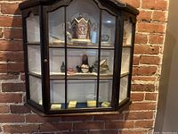 Front view of dark wood wall display case mounted on brick wall showing multiple shelves with memorabilia and figurines inside.