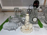 Shot of the lot showing Waterford Crystal paperweights including a round bowl-like one, an etched rectangular USA paperweight with a chip, a faceted glass clock, two clear glass bowls, and the Lenox lighthouse figurine.