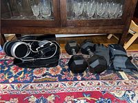 Photo showing headphones, iPod with charging cord inside a black pouch, four hex dumbbells, and two pairs of winter gloves on a patterned carpet.