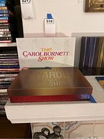 Photo showing the outer white slipcover with The Carol Burnett Show title in colored text, the collector's box behind it with a bronze and red design.