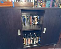 Wide angle photo showing two shelves within a dark wood cabinet filled with various DVD cases.