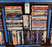 Top view of DVD collection in plastic cases showing titles including Borat, The Laugh Out Loud, Gentleman Prefer Blondes, Milton Berle, Rowan Atkinson, The Omen, Hannibal Lecter, Mr. Bean, Will & Grace, and others.
