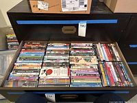 Photo of a drawer full of DVDs showing an assortment of titles in cases arranged horizontally.