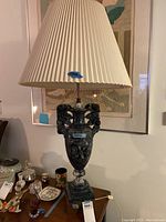 Full view of lamp on table showing carved marble base, rose handle details, and pleated shade