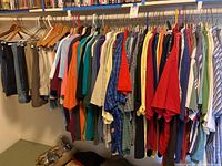 Men's shirts, t-shirts, and casual tops hanging on rod with colored hangers, showing variety of colors and fabrics.