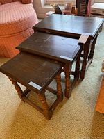 Three wooden nesting tables stacked showing top surface and turned legs with scratches.