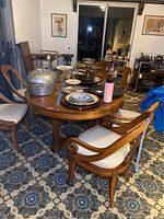 Full view of wooden dining table with one leaf in center, surrounded by chairs, placed on patterned floor.