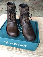 Front view of pair of brown leather Ariat boots on top of branded blue Ariat box with logo.