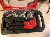 Red Arrow rivet gun with black handles placed inside a black molded insert inside a red plastic carrying case with four small bags of assorted silver rivets above gun