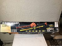 Box showing Black & Decker cordless hedge trimmer, details including 10 inch saw blade, tilting feature, and identification as cordless model.