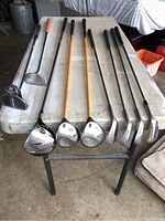 Photo of 10 golf clubs laid on a white table showing club heads and shafts.