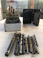 Various sizes of metal drill bits with some titanium-coated in a white metal case.