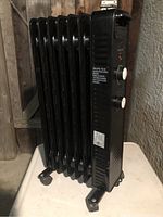 Side view of black oil-filled radiator heater showing vertical fins and wheels