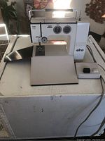 Front view of the Elna sewing machine including foot pedal and foldable surface, showing overall condition and controls.