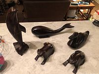 Full set of five hand carved wooden statues on a table showing dolphin, whale, two frogs, and duck.