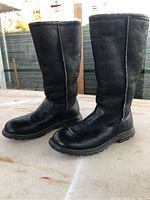 Side view of tall black leather boots showing sock-like fleece lining at opening and slightly worn leather on toes and sides.
