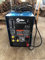 Front panel view of Miller Thunderbolt AC/DC welding power source showing amperage chart, connectors and warning labels