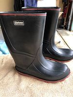 Side view of black Mudd rubber boot with red sole showing logo and overall design.