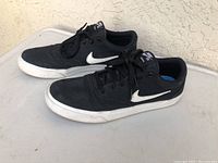 Pair of black Nike SB Charge men's shoes, size 11, viewed from side angle showing white Nike swoosh and white rubber sole with light signs of wear.