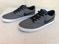 Left side angle view of the Nike SB Check men's shoe, showing grey fabric upper, black swoosh, white sole, and black laces.