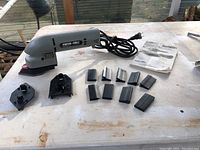 Porter Cable profile sander on a table with multiple black sanding attachments and user manual laid out beside it.