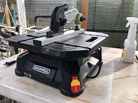 Front right angle view of Rockwell Roadrunner Table Jig Saw on a white table showing the on/off switch and the blade safety guard with green wheel.