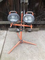 Dual halogen shop lights mounted on an orange adjustable tripod stand, shown folded with a short height.