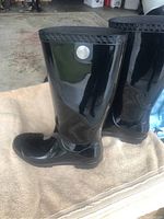 Side view of black glossy Ugg rain boot showing logo medallion and patterned top edge.