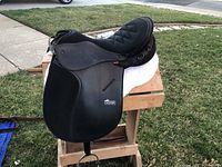 Right side view of black leather saddle on wooden stand showing flap, knee roll, stirrup iron and Ulster logo