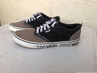 Side view of men's Vans low-top sneaker with white laces, black and gray color panels, and Vans logo on midsole around the shoe.