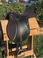 Right-side view of black Wintec synthetic English saddle on wooden stand, showing stirrup irons and leathers attached.