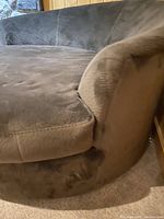 Side angle view of the brown cuddler chair showing seat cushion and curved armrest.
