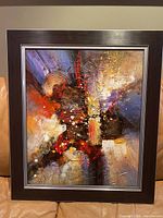 Front view of one framed abstract painting with dark wood frame and silver detailing, showing vibrant textured paint in red, black, blue, gold, and white colors.