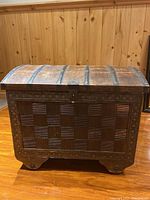 Front view of the wooden chest showing the basket weave pattern and metal straps on the domed lid.