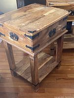 Side view of one teak side table showing wood grain, drawer, black metal hardware, and lower shelf.