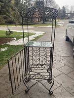 Full view of brass wine rack with metal scrollwork, glass top shelf, and open door revealing bottle holders inside.