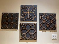 Four wooden plaques on wall, showing all different gold geometric patterns on black wooden backgrounds.