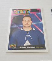 Portrait-style Upper Deck hockey card showing Auston Matthews in blue Maple Leafs jersey with neon geometric background.