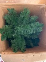 Artificial Christmas tree branches inside a cardboard box, showing green synthetic needles and typical branch structure.