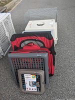 Multiple collapsible dog crates stacked outside, showing variety of materials and designs including plastic, wire mesh, and fabric.