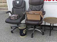Two adjustable rolling office chairs, one black and one dark brown, with a cardboard box on one chair, a Moroccan style round tray table, and a University of Pittsburgh branded office trash can below chairs.
