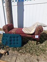 Red upholstered Queen Anne style roll arm bench with curved legs outdoors on grass.