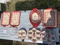 Photo of the bakeware set showing oval casseroles with lids, rectangular trays, muffin pans, and serving trays featuring the Old World Cranberry pattern.